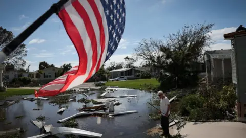 Getty Images A man cleans debris from Hurricane Ian with American flag waving through.