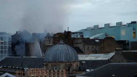 Reuters Firefighters continue to battle the fire as dawn breaks over Glasgow