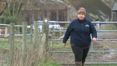 BBC Florence Mannerings walks through a farm gate surrounded by muddy fields with her dog ahead of her