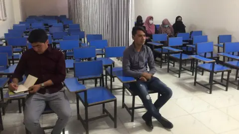 University students sit in a classroom with a curtain between the male and female students