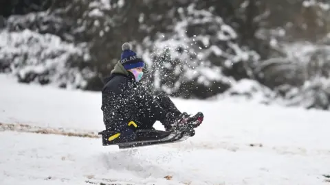 Getty Images A woman wearing a mask rides a sledge down a hill on 29 December 2020 in Newcastle-Under-Lyme, England