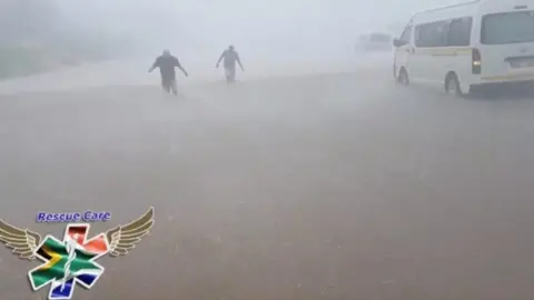 Rescue Care via Reuters People wade through flood water in strong winds and rain next to submerged vehicles on a road during stormy weather in Durban, South Africa , 10 October 2017