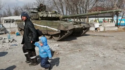 A local resident walks with a child past a tank of pro-Russian troops in the besieged city of Mariupol