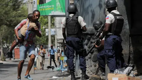 Reuters A man carries his son as they look for cover after leaving school amid gang violence in Port-au-Prince, Haiti March 3, 2023.