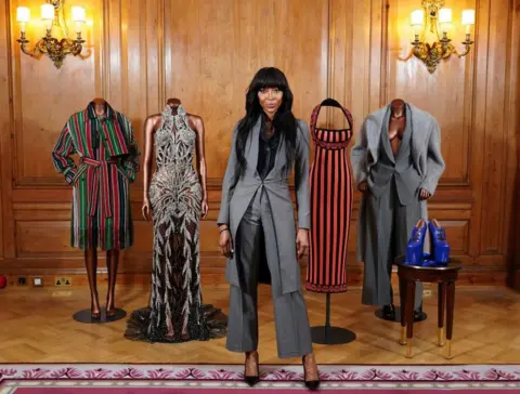 IAN WEST / PA MEDIA Naomi Campbell stands in front of mannequins wearing her outfits