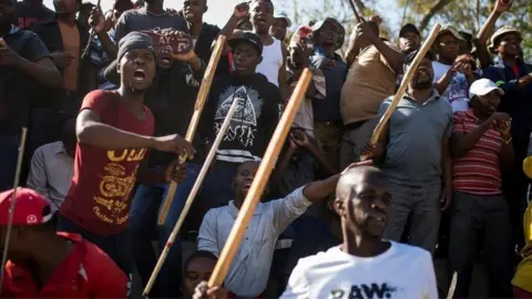 Getty Images A group of Zulu men residing at the Jeppe Hostel shout and wave sticks during a speech given by the Police Minister General Bheki Cele in JeppesTown, on 3 September 2019 in Johannesburg.