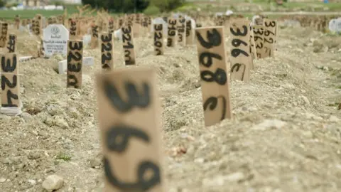 Goktay Koraltan/BBC Rows of anonymous graves with makeshift, numbered markers where victims of the quake are buried