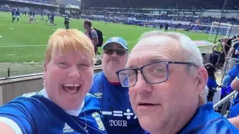 Steve Kirby Nina and Gary Battle, alongside Steve Kirby pitch side at Portman Road, all wearing their Ipswich Town replica kits.