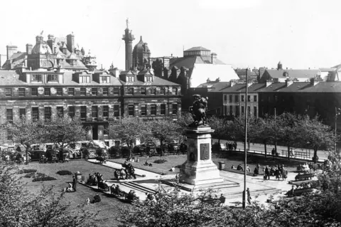 Newcastle Local Studies Library/Tyne Bridge A black and white picture of a a town square with a statue in the middle surrounded by terraced homes