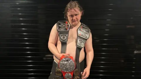 Official Charts Lewis Capaldi comically posed with five WWE belts to mark his five number ones