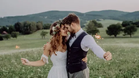 Getty Images A man and a woman at their wedding holding sparklers in a field