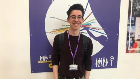 Male standing in front of a poster looking at the camera.