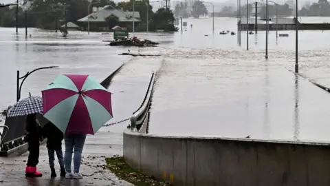 Getty Images Two people observe a flooded bridge