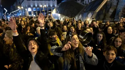 Getty Images Women in Spain shout and make noise by hitting pots and pans as they mark the start of the International Women's Day in Sol Square, 8 March 2020