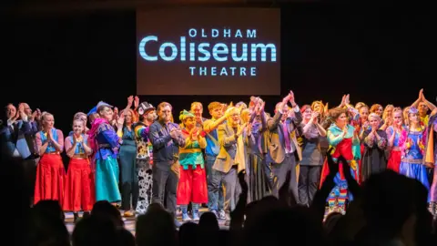 Darren Robinson A crowd of performers gathered on the Oldham Coliseum stage in various costumes as the crowd applaud