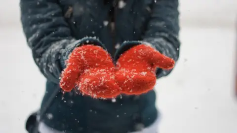 A woman wearing red gloves stands in the snow