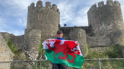 BBC Will Renwick holding a welsh flag at Conwy castle