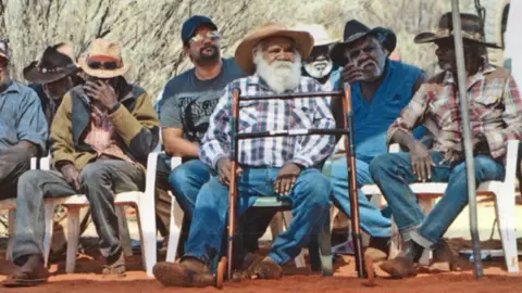 RAMETH THOMAS/ CENTRAL LAND COUNCIL Rameth Thomas sits with other traditional owners of Uluru