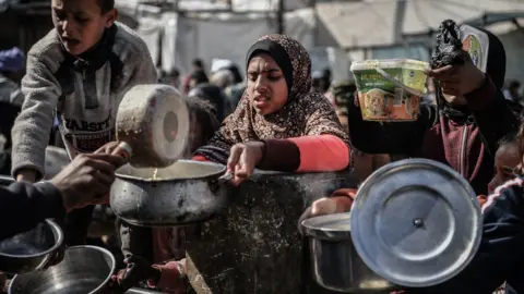 Getty Images Gaza residents receiving food from a charity's open air soup kitchen