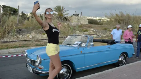 EPA A Lebanese woman takes a selfie posing next to a 1968 Peugeot 404 convertible during the Classic Cars Show in Beirut