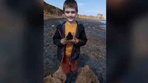 Peter Shelton Sammy Shelton holding a shark's tooth on a beach