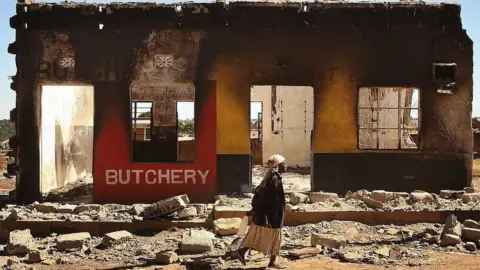 Getty Images A woman walks past a destroyed butcher's shop at Burnt Forest on January 6, 2008 near Eldoret, Kenya.
