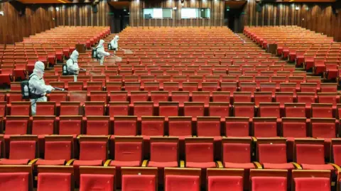 Getty Images staff members spraying disinfectant at a theatre as it prepares to reopen.