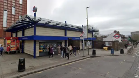 Google StreetView image of the entrance to Colindale Tube station, with people walking past