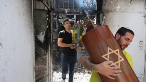 EPA Men take out a Torah scroll from a burned synagogue in Lod, Israel (12 May 2021)