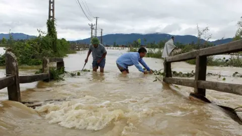 AFP/Getty Images This picture from the Vietnam News Agency taken on 11 October 2017 shows men wading through a flooded area in the central province of Nghe An