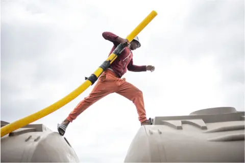 MICHELE SPATARI/ AFP A man holding a yellow pipe walking on top of a municipal tank truck.