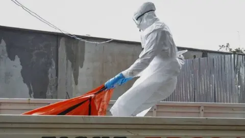 EPA A Liberian health worker in a burial squad drags an Ebola victim's body for cremation in Monrovia (13 October 2014)