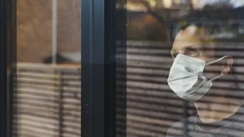 Getty Images man looking through window wearing mask