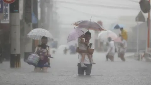 Kyodo via Reuters Local residents walk in a road flooded by heavy rain in Kurume, Fukuoka prefecture, western Japan