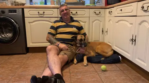 Edd Smith/BBC man sitting on floor with dog next to him