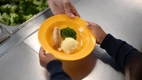 Getty Images Schoolchild takes plate of food from chef