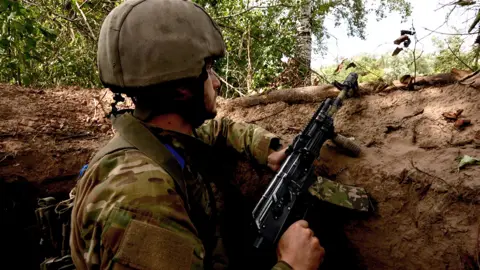 BBC Ukrainian soldier stands watch at a river observation post