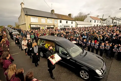 PA Media Mourners walk beside the hearse as the cortege arrives at St Brigid's Church, Mountbolus, Co Offaly, Ireland, for the funeral of Ashling Murphy, on 18 January 2022