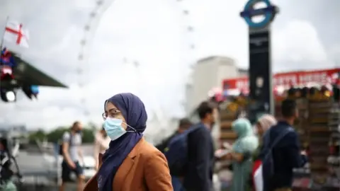 Reuters People, some wearing protective face masks, walk over Westminster Bridge