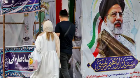 Getty Images People walk past a poster of Ebrahim Raisi during the Iranian presidential election on Iran's Kish Island (18 June 2021)