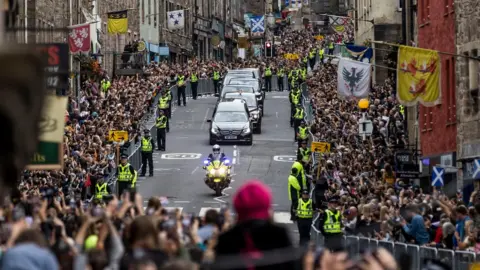 PA Media Members of the public gather on the Royal Mile in Edinburgh to watch the hearse carrying the coffin of Queen Elizabeth II passes by