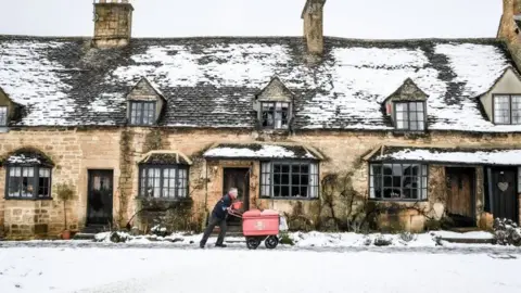 PA A postman pushing his trolley through snow in Broadway, Worcestershire