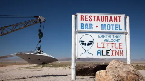 Getty Images Sign for Little A'Le'Inn and flying saucer hanging from tow truck, Rachel, Nevada