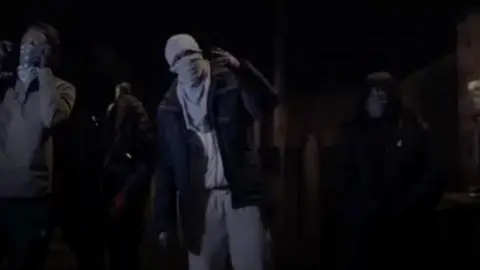 BBC Men wearing facemasks rapping in a drill video