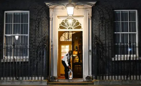 EPA A custodian places a lit candle outside 10 Downing Street to mark one year of Covid-19 and to honour those who lost their lives to Covid-19 in London, 23 March 2021.