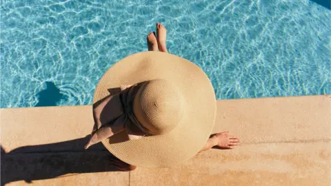 Getty Images Sun bather in wide-brimmed hat sits next to pool