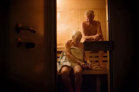 Moa Karlberg An elderly couple sit in a sauna.