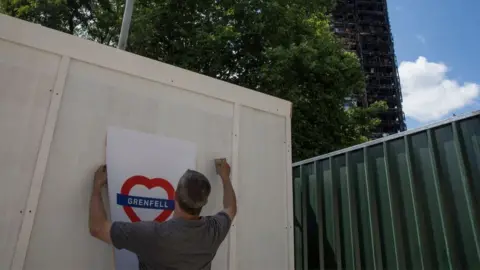 Getty Images man puts up heart shaped grenfell poster in the shadow of the burnt out tower