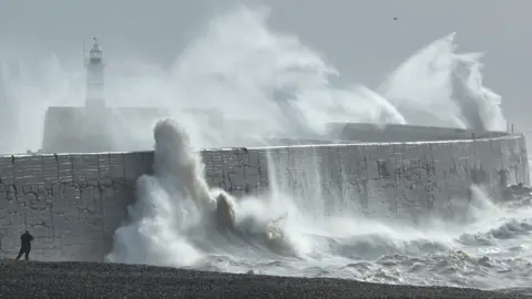 A person views as large waves hit the harbour wall at sunrinse during Storm Isha in Newhaven, southern Britain, on 22 January 2024