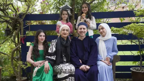 National Portrait Gallery/Ancestry Eid al-Fitr, the celebration that marks the end of Ramadan on the Bank Holiday Monday 2nd June 2022. Everyone is wearing something new for the Eid which they have selected themselves reflecting their distinct personalities. It is a very British Muslim family photo taken in the Buckinghamshire garden of my father-in-law, the photographer Peter Sanders who took the photographs.